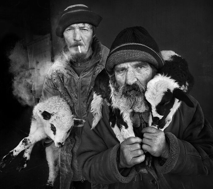 Two men in winter clothing holding lambs, illustrating the resilience and beauty of everyday people.