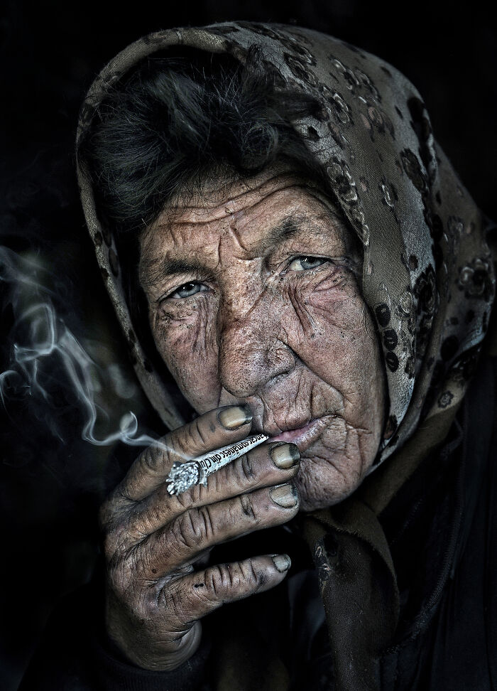 A resilient elderly woman with a headscarf smoking, capturing the beauty and resilience of everyday people.