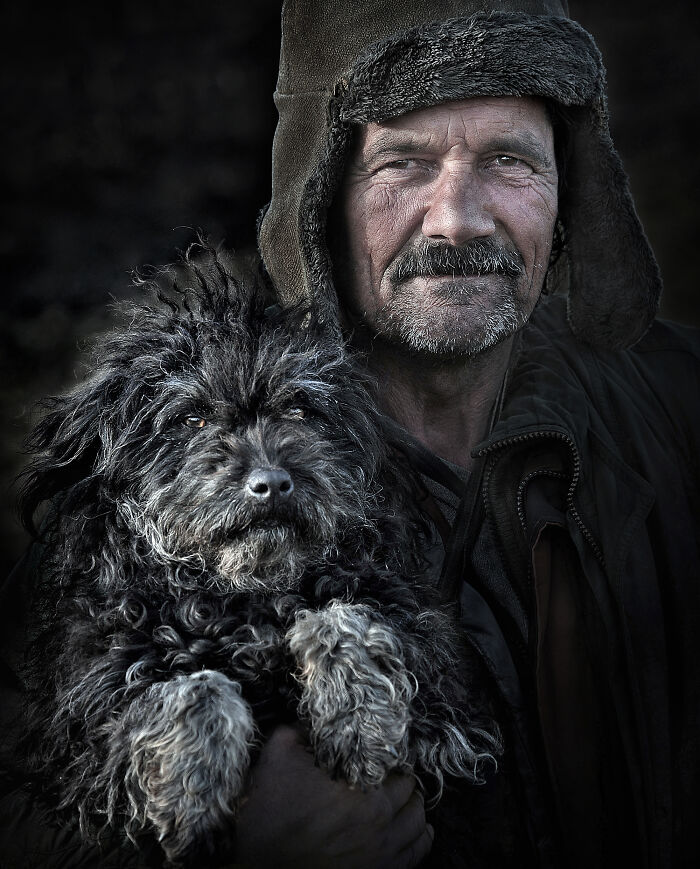 Man in warm hat holding a fluffy black dog, showcasing resilience and beauty of everyday people.