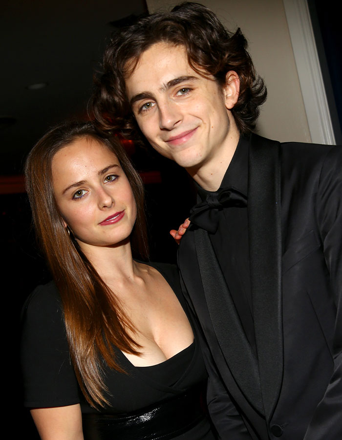 Brother and sister in formal attire at an event, both smiling, with the sister looking confidently at the camera.