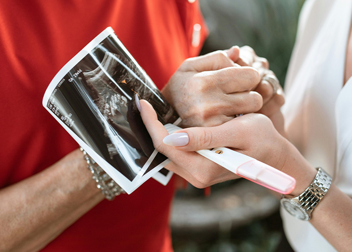 Two people holding a sonogram and pregnancy test, discussing a gift that feels creepy and invasive.