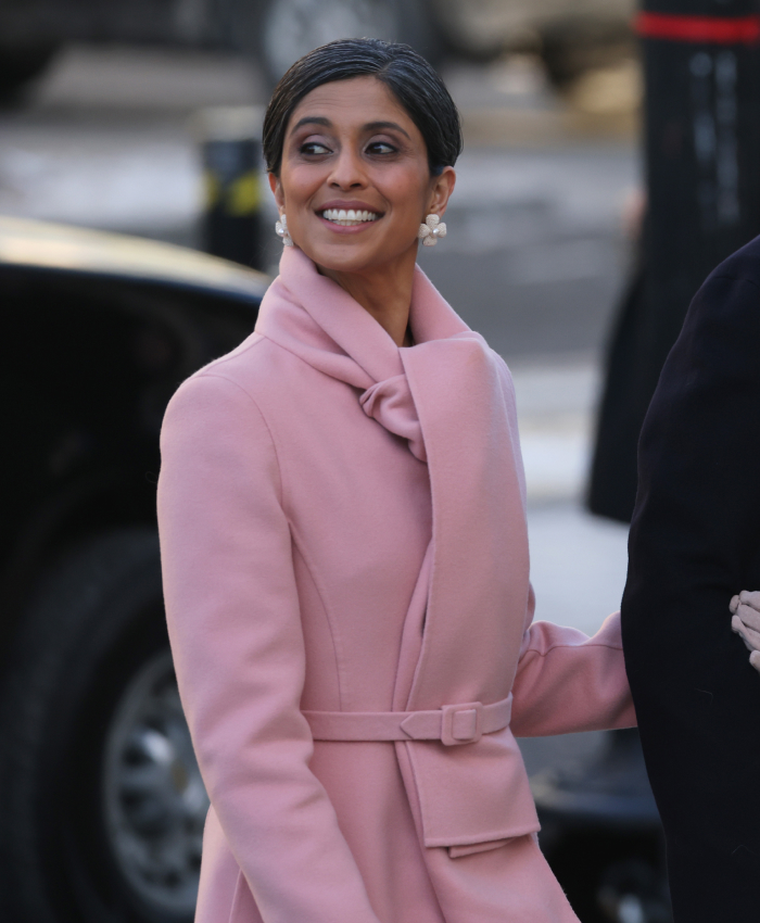 Person in a pink coat at a presidential inauguration, smiling and wearing pearl earrings.