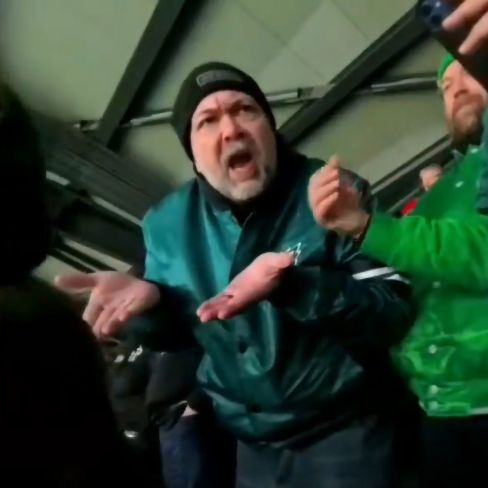 Abusive Eagles fan gesturing angrily at a stadium, wearing a green jacket and black beanie.