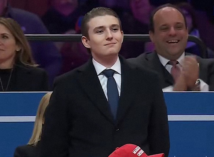 Barron Trump in formal attire stands at the inauguration, surrounded by applauding attendees.