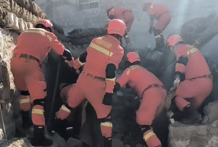 Rescue workers in orange uniforms searching rubble after a 7.1 earthquake, illustrating disaster prediction challenges.