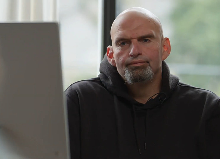 A senator wearing casual attire, including a hoodie, sits indoors in a relaxed setting.