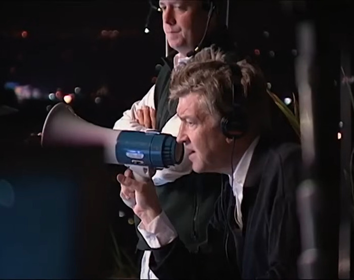 Director using a megaphone on set, wearing headphones, involved in production work, with focus on directing "Twin Peaks.