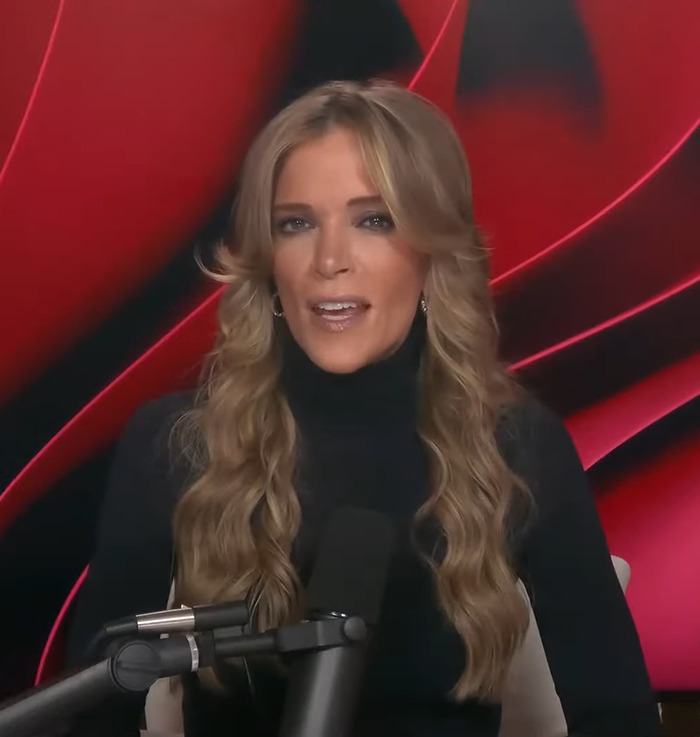 A person speaking into a microphone, wearing a black top, against a red background; discussing female firefighter leaders.