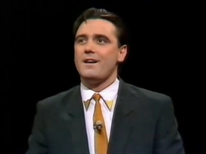 Actor from 'Whose Line Is It Anyway?', wearing a suit and tie, appearing on stage.