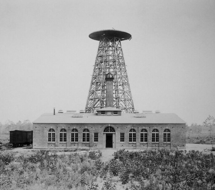 Historical invention: a large, metal tower with a wide circular top, attached to a brick building in an open landscape.