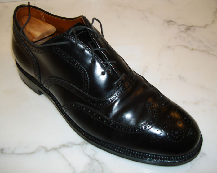 Shiny black leather dress shoe with detailed stitching on a marble surface, illustrating interesting facts from community insights.