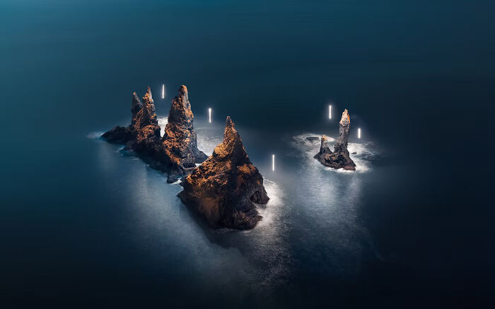 Dramatic coastal rock formations at night, featuring soft glowing lights from The Artist Gallery Awards.