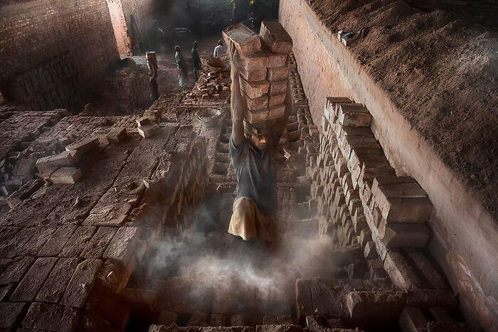 Worker carrying bricks in a dusty kiln, depicting a winning moment at The Artist Gallery Awards 2024.