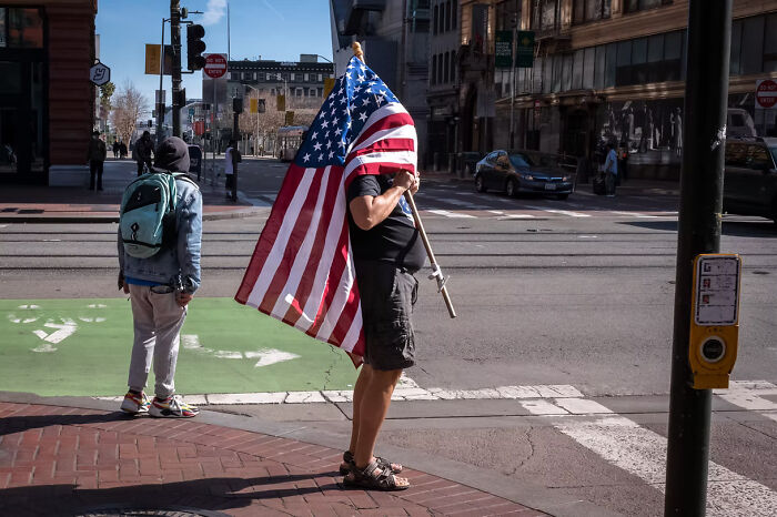 Man holding an American flag on a city street, featured in The Artist Gallery Awards 2024 winning photos.