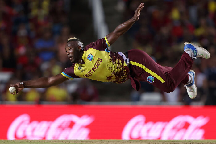 West Indies cricketer in mid-air dive during a match, capturing a winning moment in sports photography.