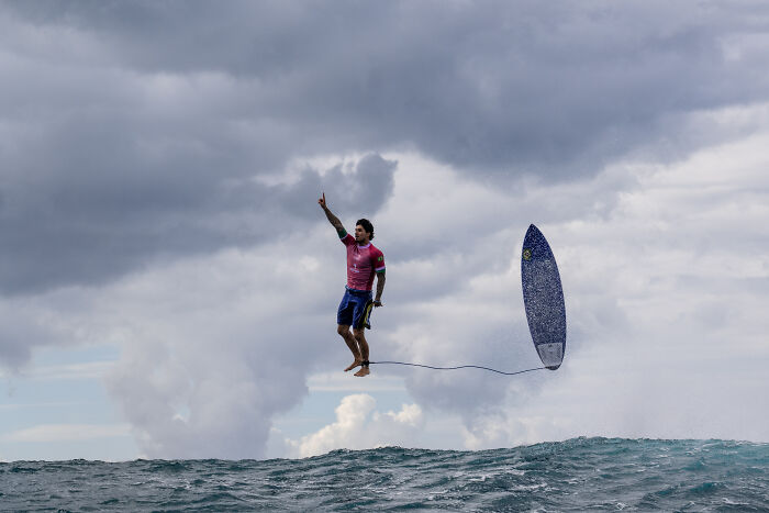 Surfer in mid-air, pointing upwards with surfboard nearby, captured in an award-winning sports photography shot.