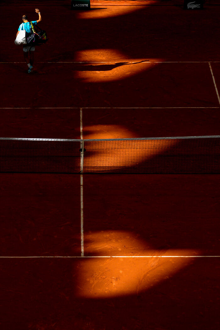 Tennis player on clay court with dramatic lighting, a winning image from the 2025 World Sports Photography Awards.