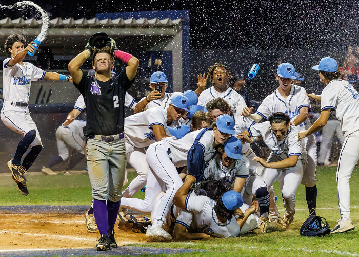 Baseball team celebrating on the field while a player from the opposing team looks dejected, captured by sports photography award winner.