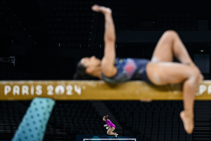 Gymnast in motion on balance beam at 2024 Paris event; sports photography award-winning moment.