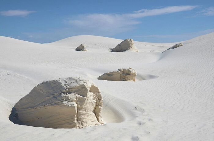 White sand dunes and rock formations under a blue sky showcasing strange natural phenomena.