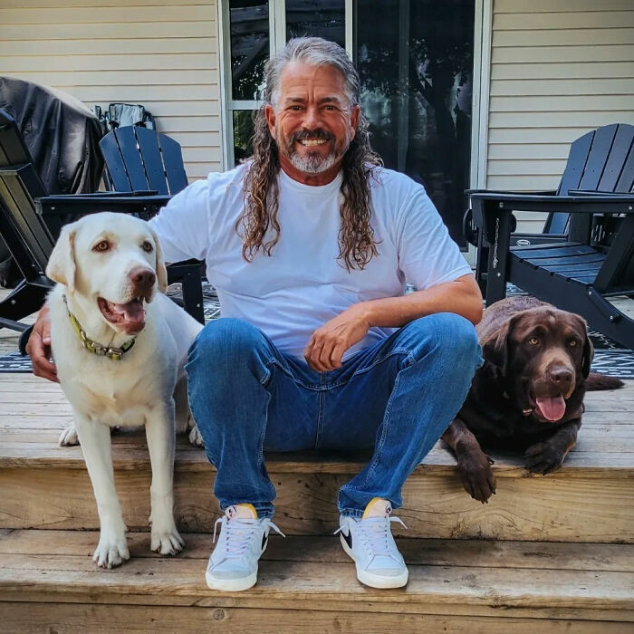 Person with mullet hairstyle sitting on steps with two dogs, embodying the "business in the front, party in the back" look.