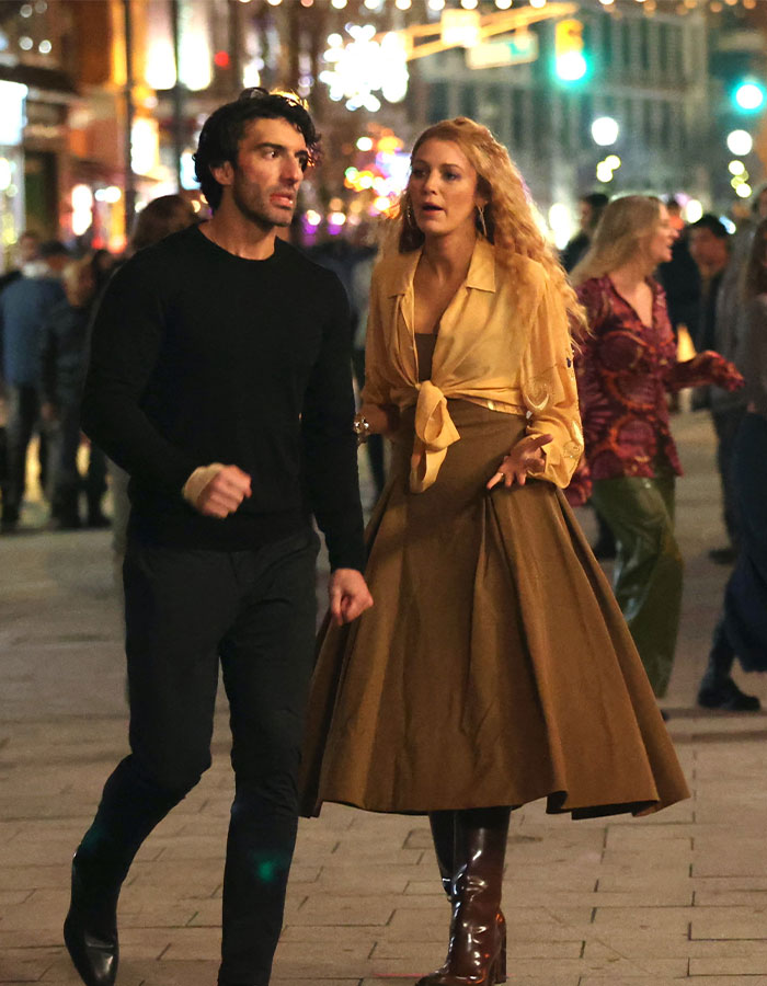 Justin Baldoni and a woman walking at night, discussing a legal matter downtown.