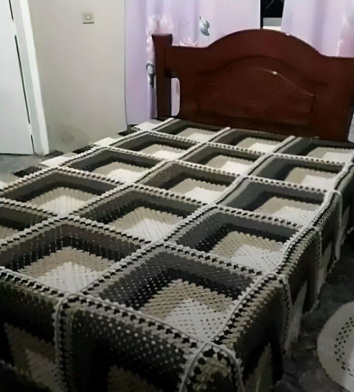 Confusing perspective of a bed with a 3D crochet blanket resembling a series of deep boxes.