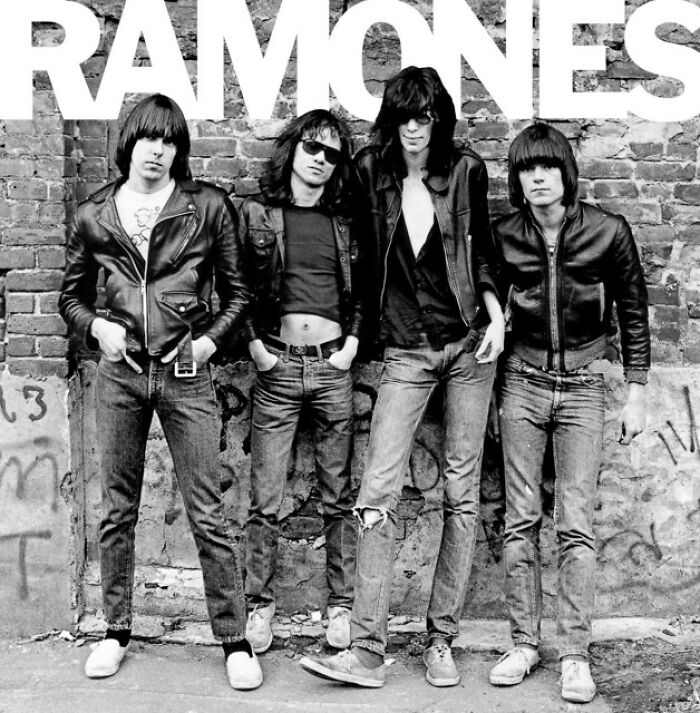 Band posing in front of a brick wall, exemplifying '70s style with leather jackets and jeans.