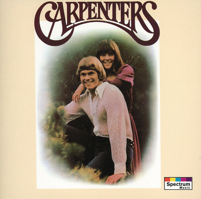 Album cover of the Carpenters, a '70s music duo, with one person seated and the other standing behind, smiling.