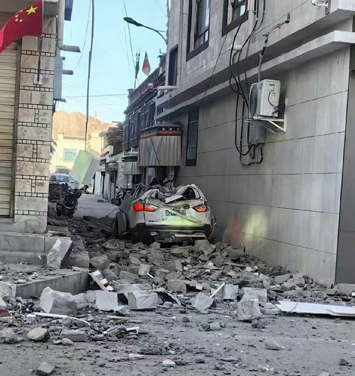 Damaged car under rubble on a street after a 7.1 earthquake impact, highlighting disaster prediction challenges.