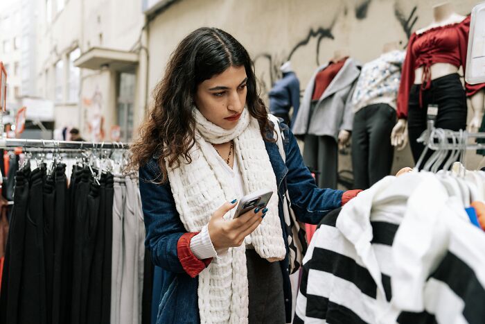 Woman using phone examining striped shirt.