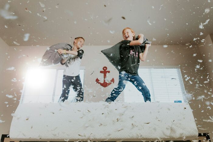 Children having a pillow fight on a bed, feathers flying around, creating a playful and chaotic scene.