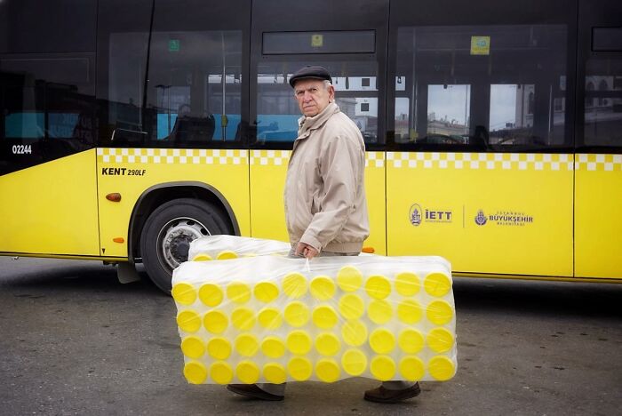 Man carrying yellow tubes, accidentally aligning with a bus design, captured by a street photographer.