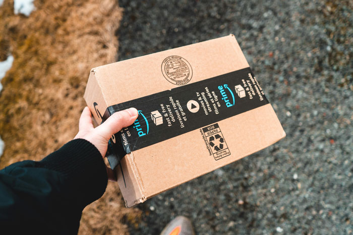 Person holding an Amazon package on a gravel path, symbolizing changes in the "Try Before You Buy" service due to AI.