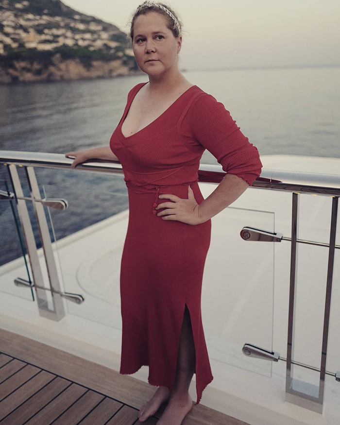 A woman in a red dress stands on a boat deck by the sea, looking thoughtful.