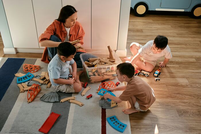 Adult and three kids playing with wooden train set on the floor, highlighting positive parenting.