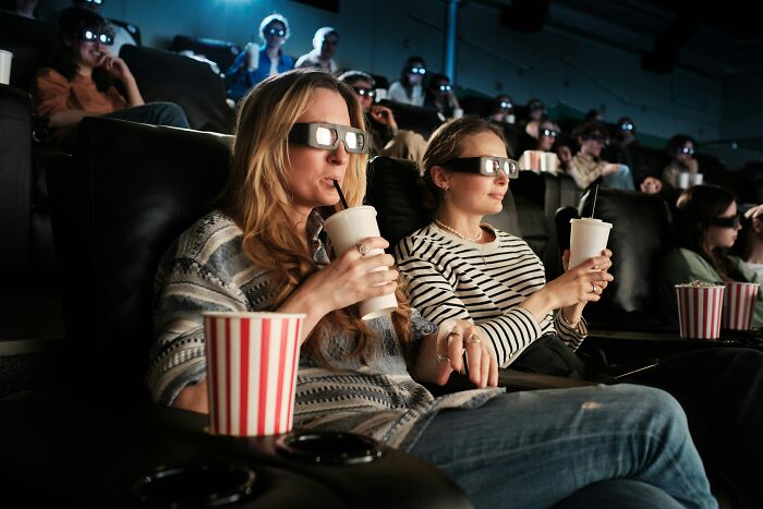 People watching a 3D movie at a theater, enjoying popcorn and soda; an experience becoming unaffordable for middle class.