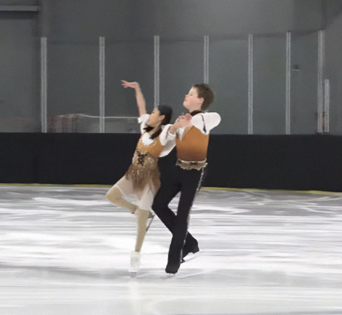 Child ice skating duo performing on the rink, dressed in coordinated outfits.