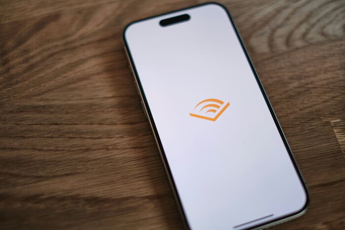 Smartphone on a wooden table displaying an audiobook app logo, representing an unethical life hack concept.