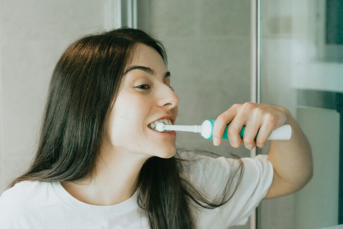 Woman using an electric toothbrush, an expensive item worth spending money on for better oral hygiene.