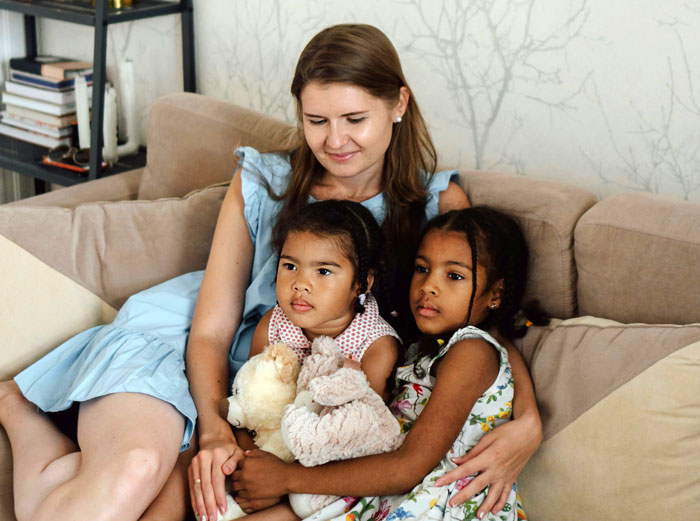 Babysitter with two children on a sofa, one holding stuffed animals, highlighting unexpected extra tasks.