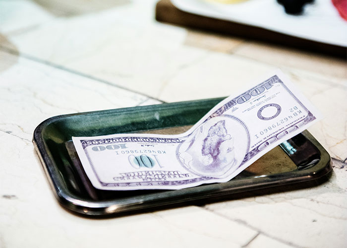 100-dollar bill on a restaurant tip tray, related to customer tipping 10% for service.