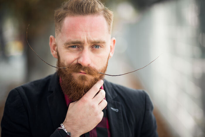 Man with a unique mustache, wearing a suit outdoors, pondering resume red flags discussed by HR specialists.