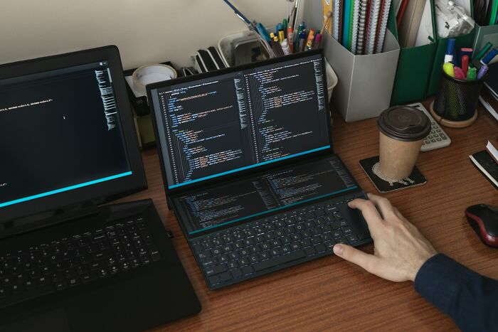 Person coding on dual laptops with coffee cup, showcasing intriguing tech facts.