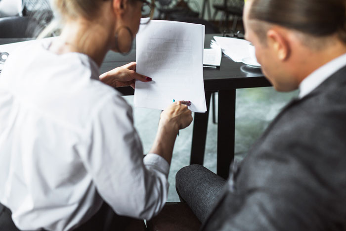 Two employees discussing a document related to bereavement and miscarriage policies in an office setting.