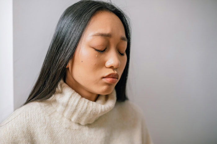 Woman in a cream sweater with teary eyes, contemplating work-life challenges and employment concerns.