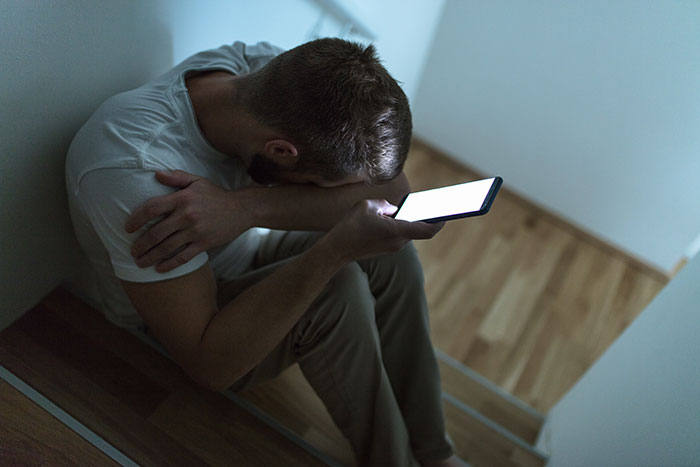 Man sitting on stairs, looking emotional while holding a phone, related to love confession from a friend.