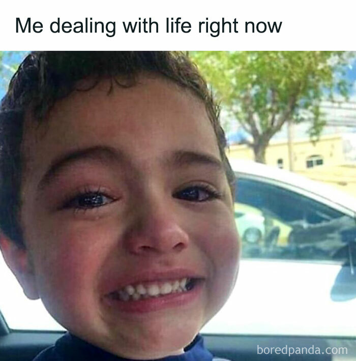 Young child making a strained smile while crying, sitting in a car, capturing an introverted feeling.