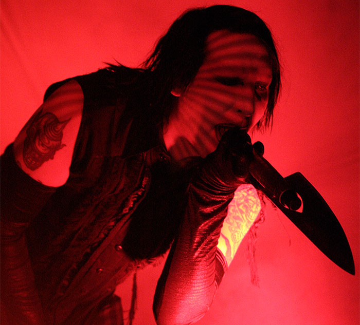 Musician performing on stage with dramatic red lighting, embodying celebrity secrets and scandals theme.