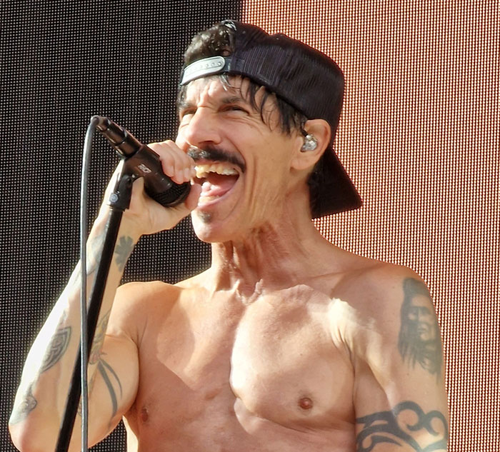 Shirtless singer on stage wearing a cap, passionately performing with a microphone, embodying celebrity secrets and scandals theme.